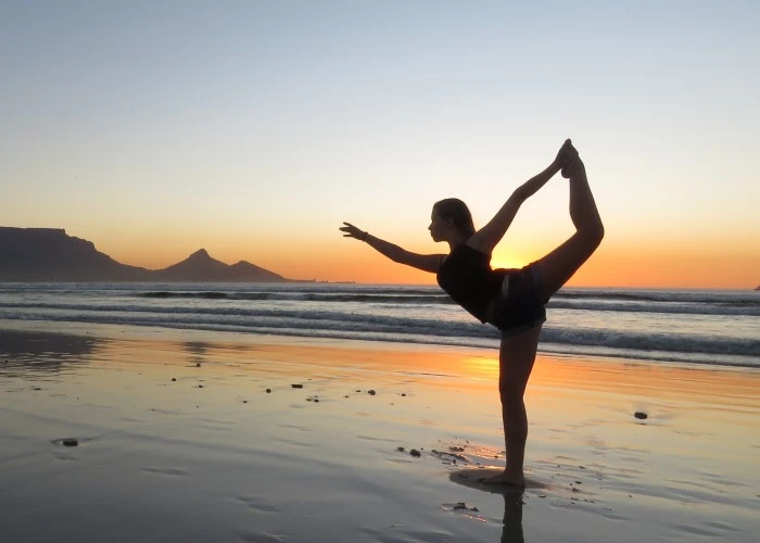 A lady doing yoga on a beach at sunset
