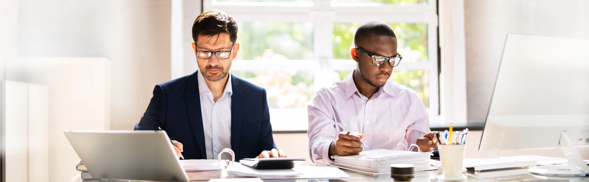 Two men in an office environment working at laptops on the same desk