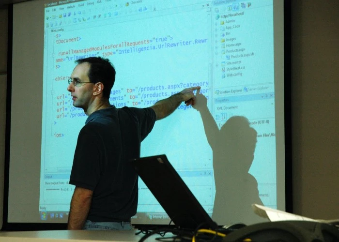 A man in front of a projection of some computer coding, pointing out what he's teaching