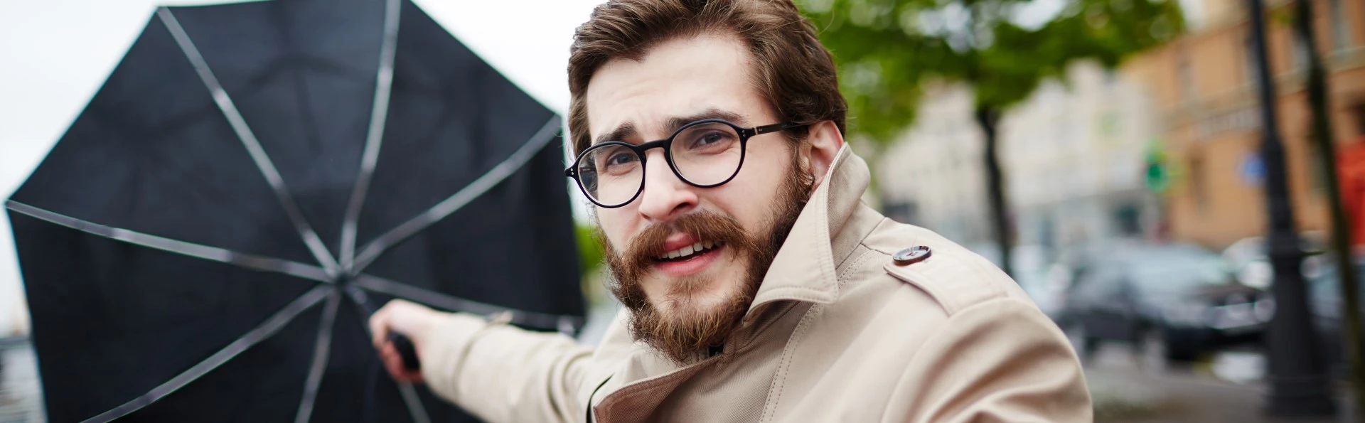 A man holds an umbrella that is being blown away