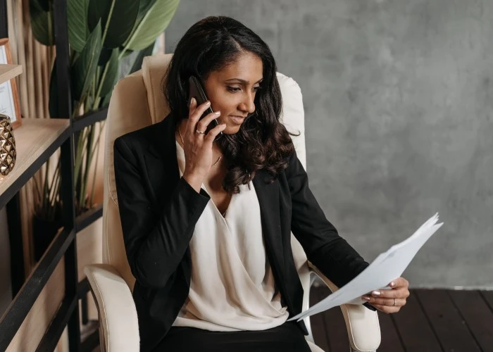 Asian lady sitting on an office chair, looking at a document whilst on the phone