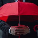 Man holding dark red umbrella signifying danger.